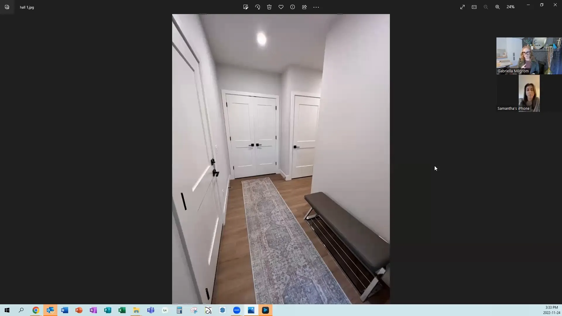 A narrow hallway with light gray walls, wooden floor, and a long rug leads to white double doors. A bench sits on the right. Neutral and modern ambiance.