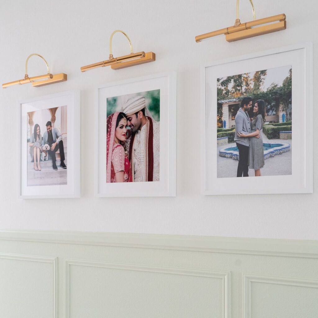 Hallway gallery wall with framed family photos, brass picture lights, classic wall moulding, and white picture frames, creating a personalized and elegant transitional interior design.