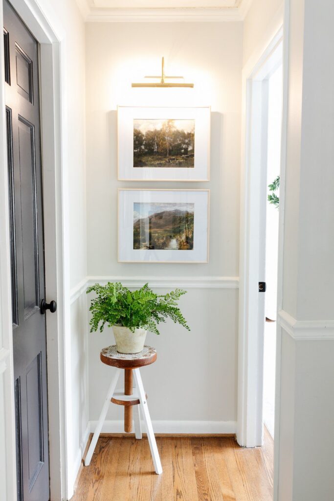 Traditional hallway design with a brass picture light highlighting framed artwork, classic wall moulding, soft neutral paint, warm oak flooring, and layered decorative styling for an elegant transitional interior.